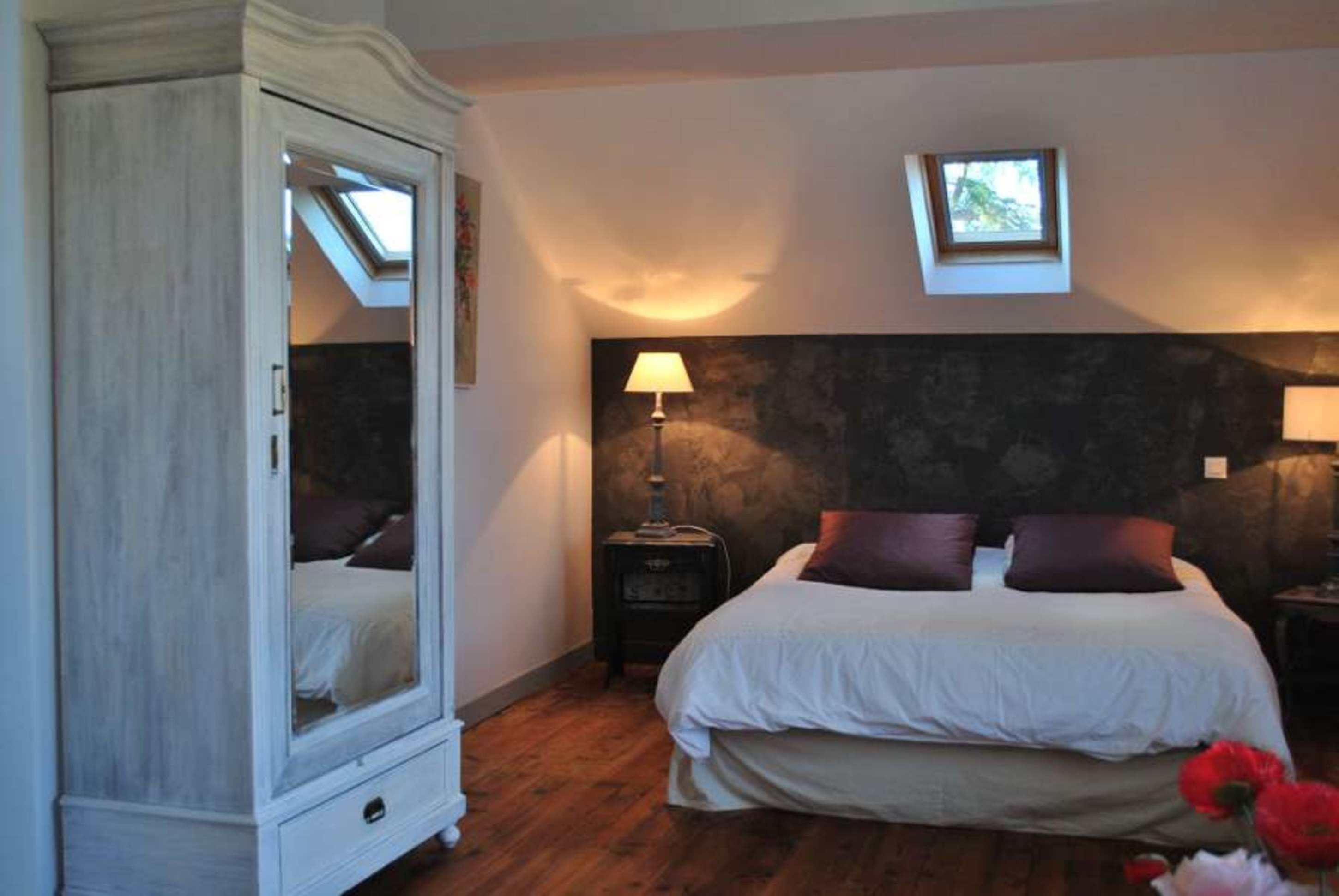 Una camera da letto con un letto grande, un armadio, un comodino con una lampada e una piccola finestra sopra il letto.