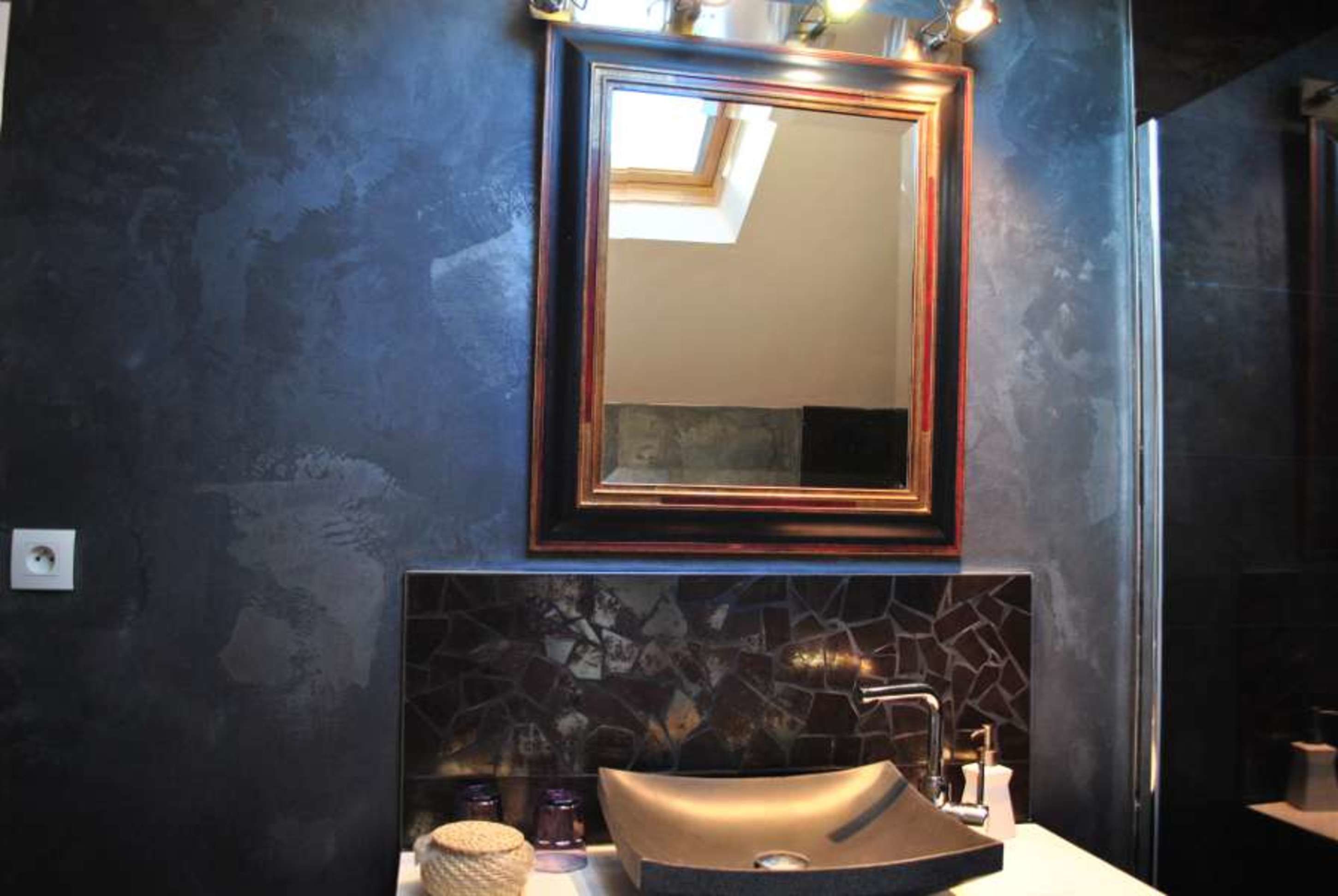 Une salle de bain avec un grand miroir, un lavabo doté d’un pare-éclaboussures en pierre et un petit objet décoratif posé sur le comptoir.