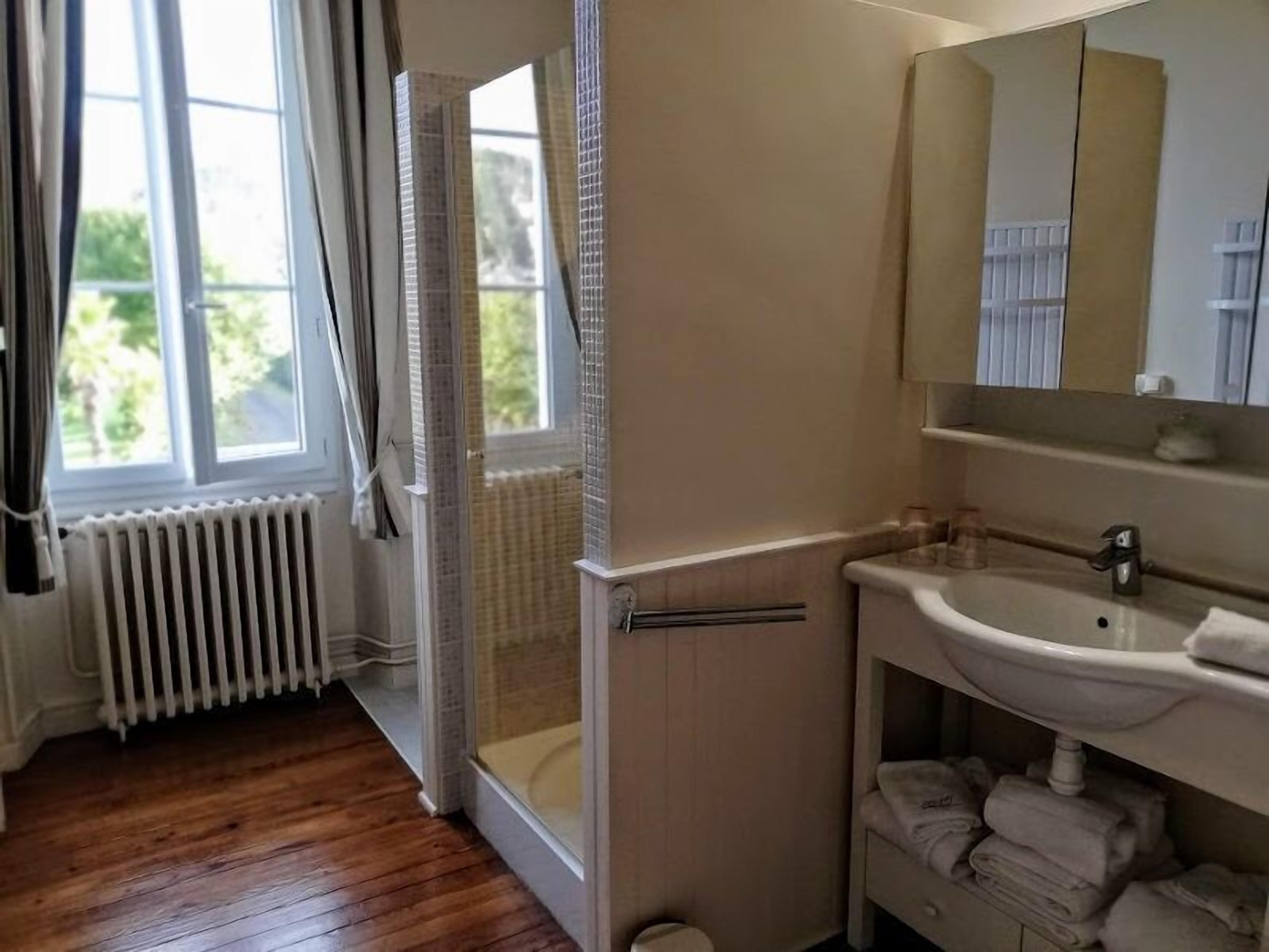 A bathroom with a bathtub, a sink, and a mirror. There is a window with curtains and a view of greenery outside.