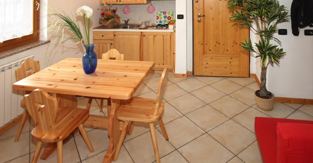 Una mesa de comedor de madera con sillas, un jarrón con flores, una planta en maceta y un cojín rojo.