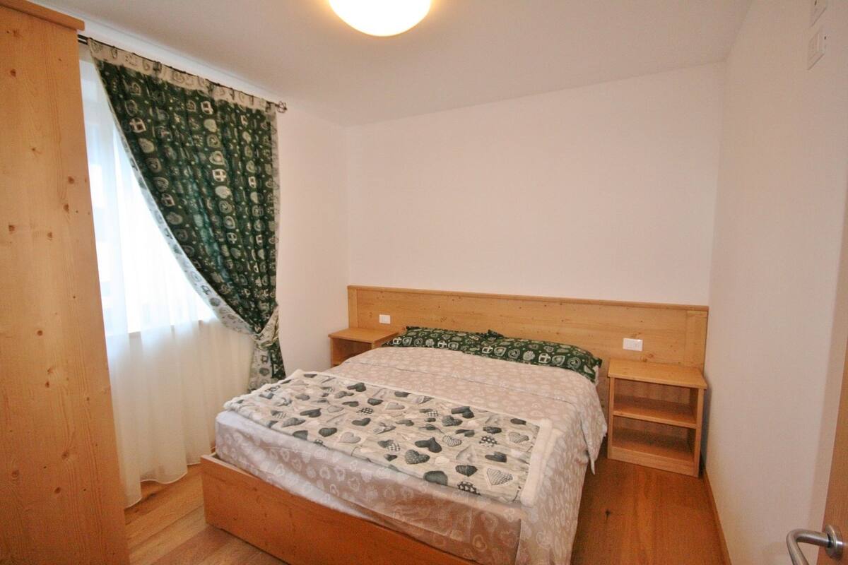 Une chambre à coucher avec un cadre de lit en bois, une couvre-lit à motifs, une table de chevet en bois et une fenêtre ornée de rideaux à motifs.