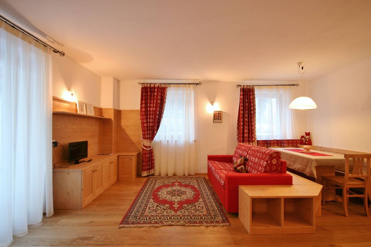 Un salon chaleureux avec un canapé rouge, des meubles en bois et un coin repas comprenant une table et des chaises.