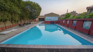 Una piscina con plataforma de baldosas, rodeada de asientos exteriores y un muro con murales.
