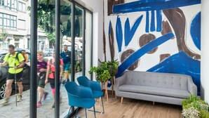 Un interior moderno con un gran ventanal, un sofá gris, sillas azules y un cuadro abstracto azul en la pared.