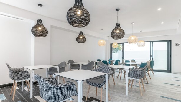 Una sala de reuniones moderna con mesas blancas y sillas estampadas, ventanas amplias y lámparas colgantes tejidas.