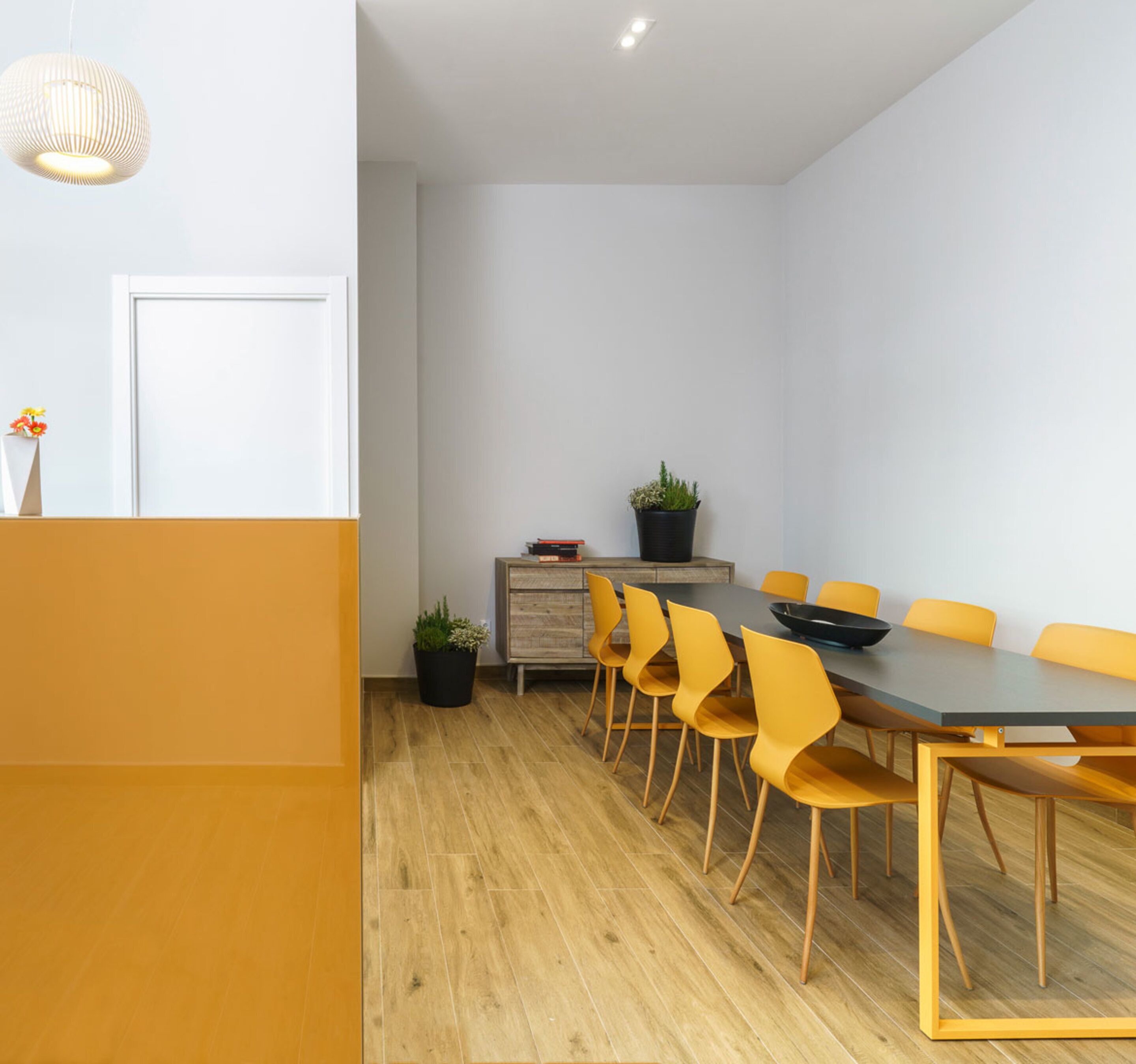 A modern dining area with a wooden table and yellow chairs, a small plant, and a white door.