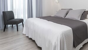Un dormitorio moderno con una cama grande, una silla y cortinas traslúcidas.
