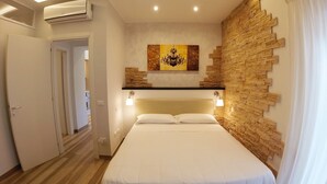 Un dormitorio con una cama, una obra de arte en la pared, una pared de acento de piedra y una puerta que da a otra habitación.