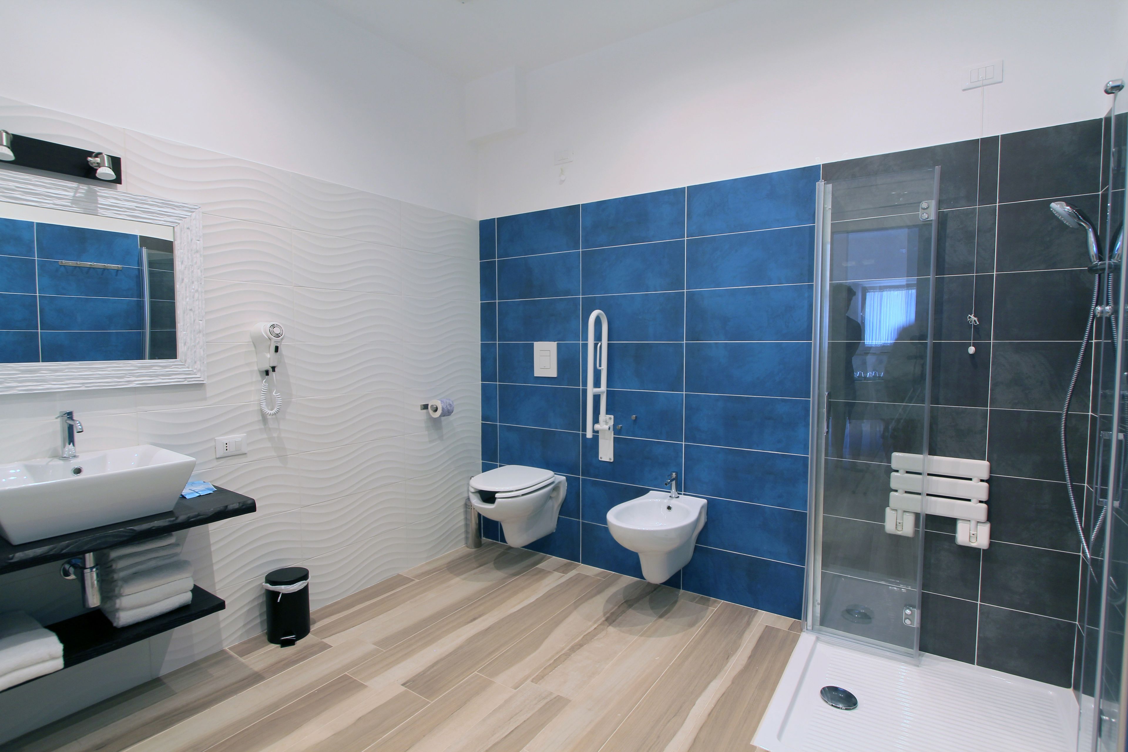 Et moderne badeværelse med stor vask, toilet, bidet og en bruseafdeling med glasvægge.