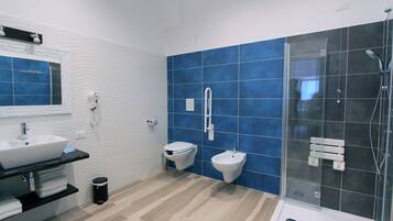 Et moderne badeværelse med stor vask, toilet, bidet og en bruseafdeling med glasvægge.