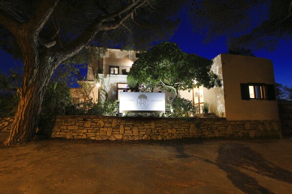 A hotel with a stone facade, a large tree in front, and a signboard.