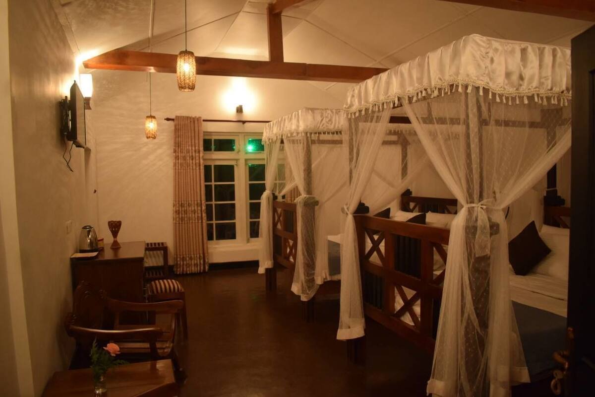 Ein Zimmer mit einem hölzernen Bett mit Baldachin, einem Holzstuhl, einem kleinen Tisch mit einer Vase und einem Fenster mit Vorhängen.