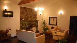 A cozy living room with a stone fireplace, a television mounted on the wall, and a chandelier. - Micklefield Bungalow (Welimada)
