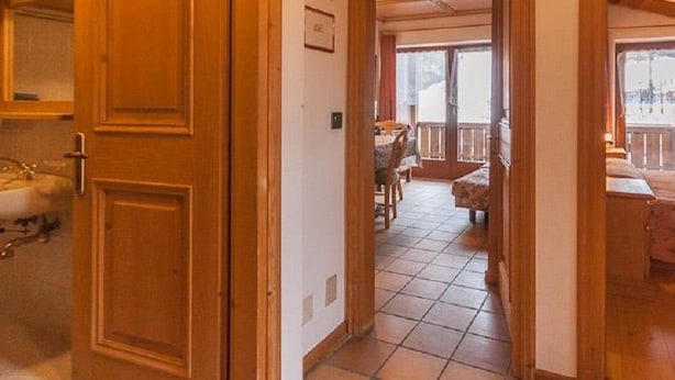 A room with a wooden door, a bathroom with a sink, a dining area with a table and chairs, and a bed with a floral bedspread.