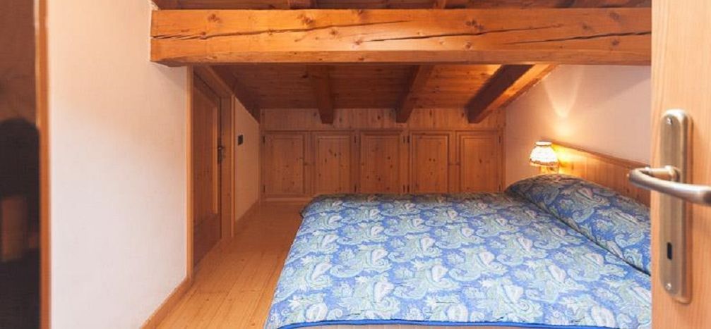 A small, cozy bedroom with a wooden ceiling and a single bed with patterned bedding.