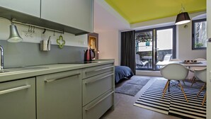 Een moderne keuken met een groen aanrecht, een waterkoker en een koffiepot. Er is een zithoek met een tafel en stoelen, en een groot raam met gordijnen.