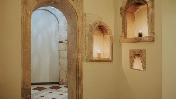 An arched doorway leading to a room with a tiled floor and a candle in a window.