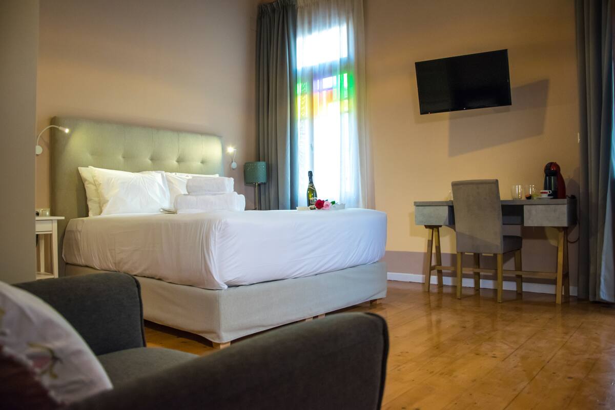 Ein Hotelzimmer mit einem großen Bett, einem Schreibtisch, einem Stuhl, einem Flachbildfernseher und einem Fenster mit Vorhängen.