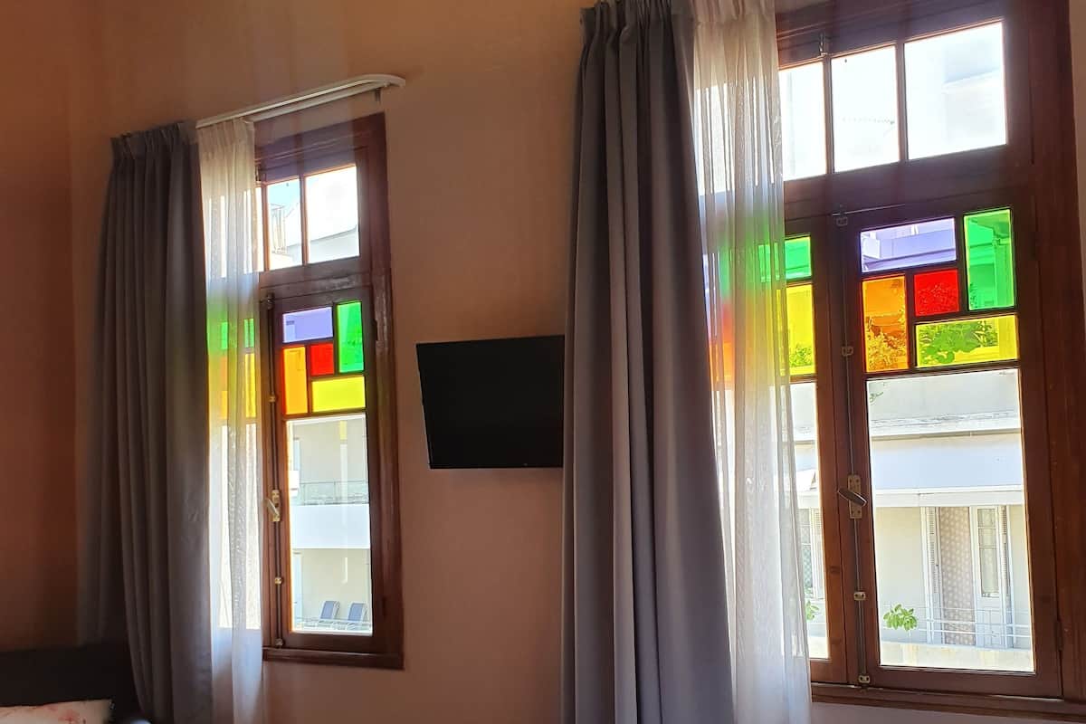 Ein Hotelzimmer mit Bett, Wandfernseher und zwei mit Vorhängen versehenen Fenstern.