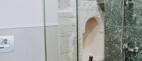 A bathroom with a glass-enclosed shower, a white sink, and a marble wall.