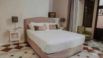 Una cama bien tendida en una habitación de hotel, con un suelo a cuadros, una mesita de noche con una lámpara y una silla.