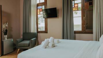 A hotel room with a bed, a chair, a TV, and a small table with a plant.