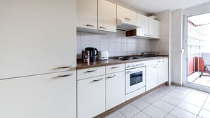 A modern kitchen with white cabinets, a gas stove, a coffee maker, and a view of the outside. - Apartment 2 Zimmer Flughafen Stuttgart (Filderstadt)
