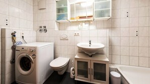 A compact bathroom with a washing machine, toilet, sink, and a cabinet with glass doors. - Apartment 2 Zimmer Flughafen Stuttgart (Filderstadt)