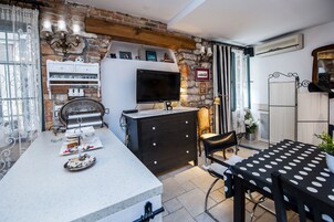 A kitchen with a stone wall, a TV, a dining table with chairs, and a small island with a sink and decorative items.