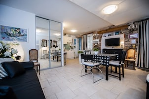 A modern living room with a black sofa, a dining table with chairs, a TV, and a kitchen in the background.