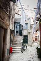 A narrow stone-paved alley with a bicycle and a flag hanging from a building.