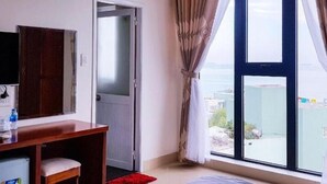 A hotel room with a large window, a desk with a chair, a television, and a door leading to another room. - Tram Anh Hotel (Quy Nhon)