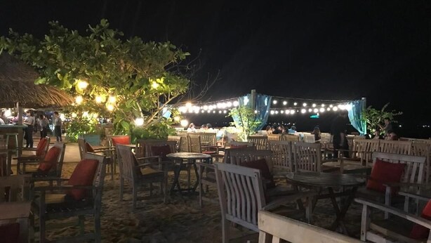 An outdoor seating area with tables and chairs, string lights, and a thatched-roof structure. - Tram Anh Hotel (Quy Nhon)