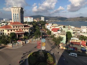 A cityscape with a prominent building with a red roof, a large fountain in the center, and a body of water in the background. - Tram Anh Hotel (Quy Nhon)