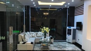 A modern living room with a marble floor, a sofa set, a glass partition, and a chandelier. - Tram Anh Hotel (Quy Nhon)