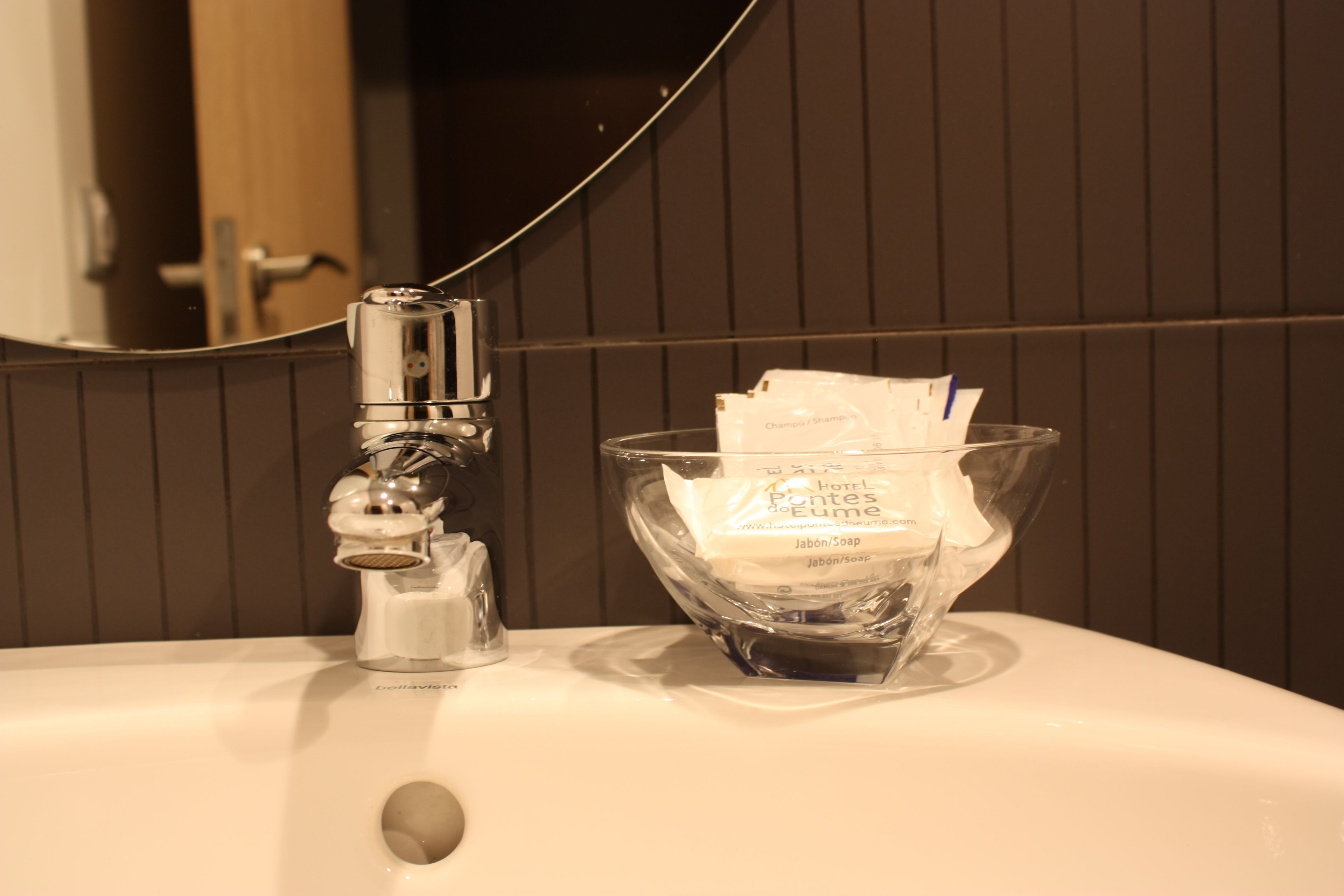 A bathroom sink with a soap dispenser and a glass bowl containing a soap packet.