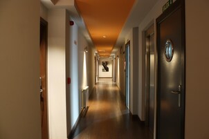 Corredor de hotel com piso de madeira, portas em ambos os lados e uma placa indicando a saída.