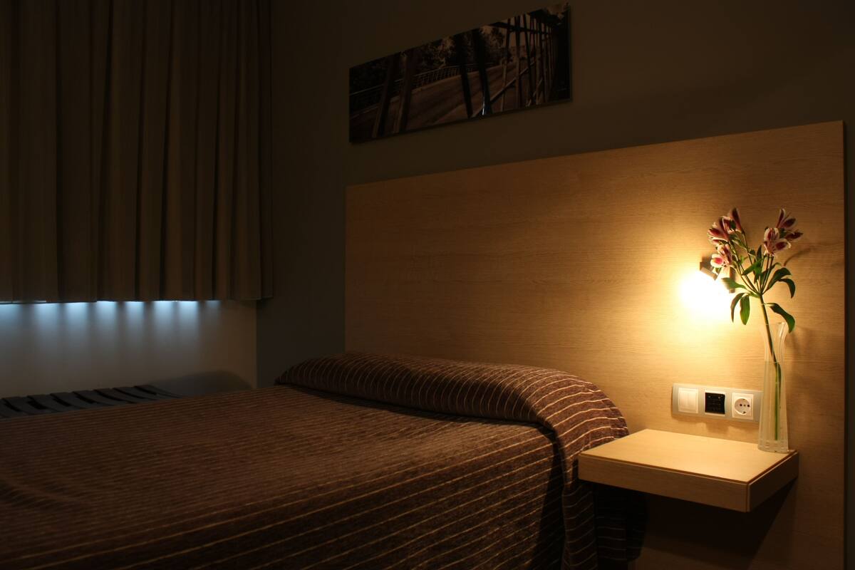 Una habitación de hotel con una cama, una mesita de noche con lámpara y un cuadro en la pared.