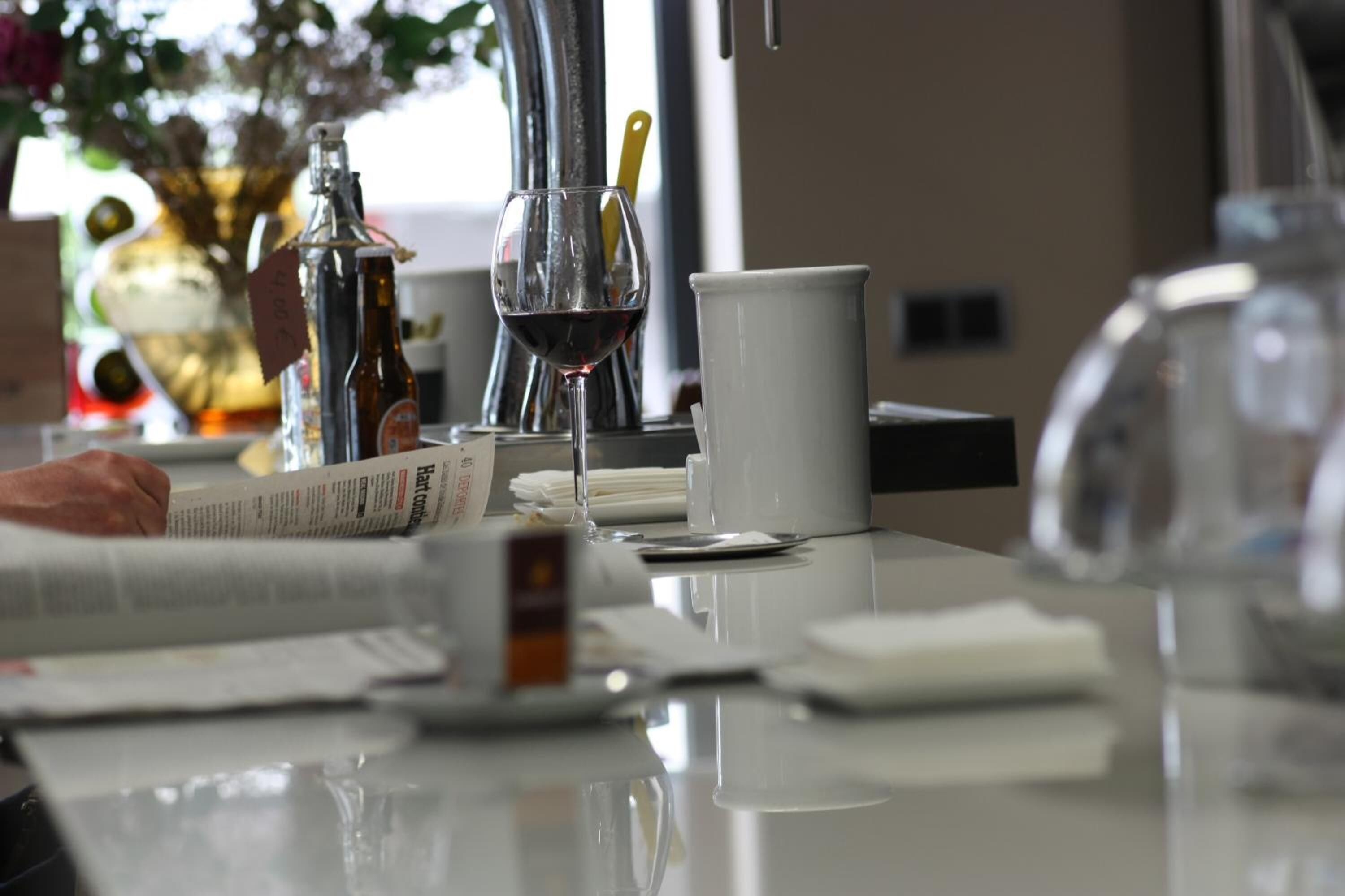 A table with a wine glass, a bottle, a white mug, and a newspaper.