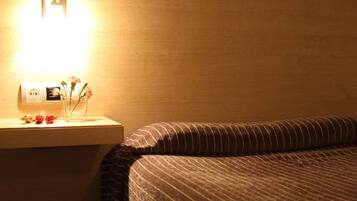 A hotel room with a wooden headboard, a bedside table with a lamp, and a nightstand with a vase of flowers.