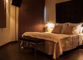 Quarto com cama, um banquinho, mesa de cabeceira e luminária na parede.