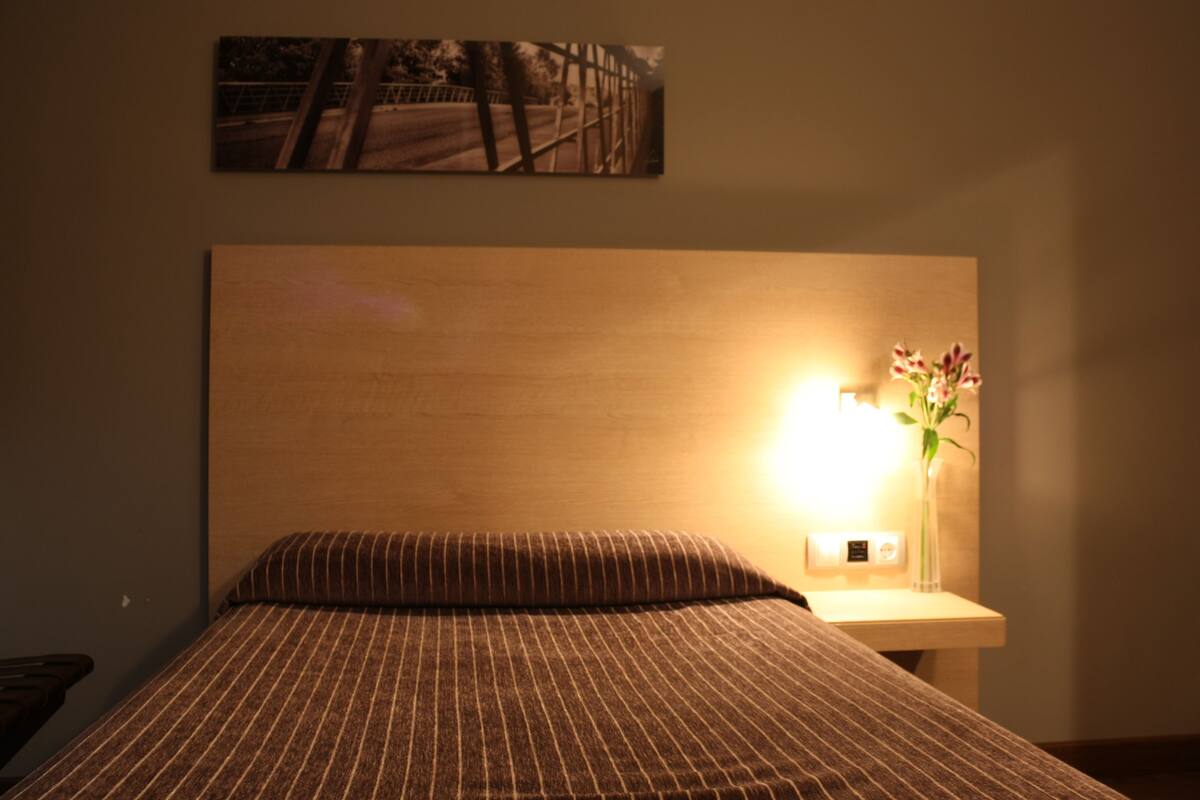 Una habitación de hotel con cama, mesita de noche con lámpara y un cuadro en la pared.