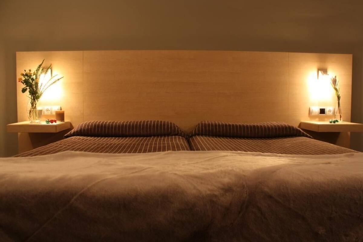 Una cama doble con cabecera de madera, dos mesitas de noche con lámparas, y un florero con flores a cada lado.