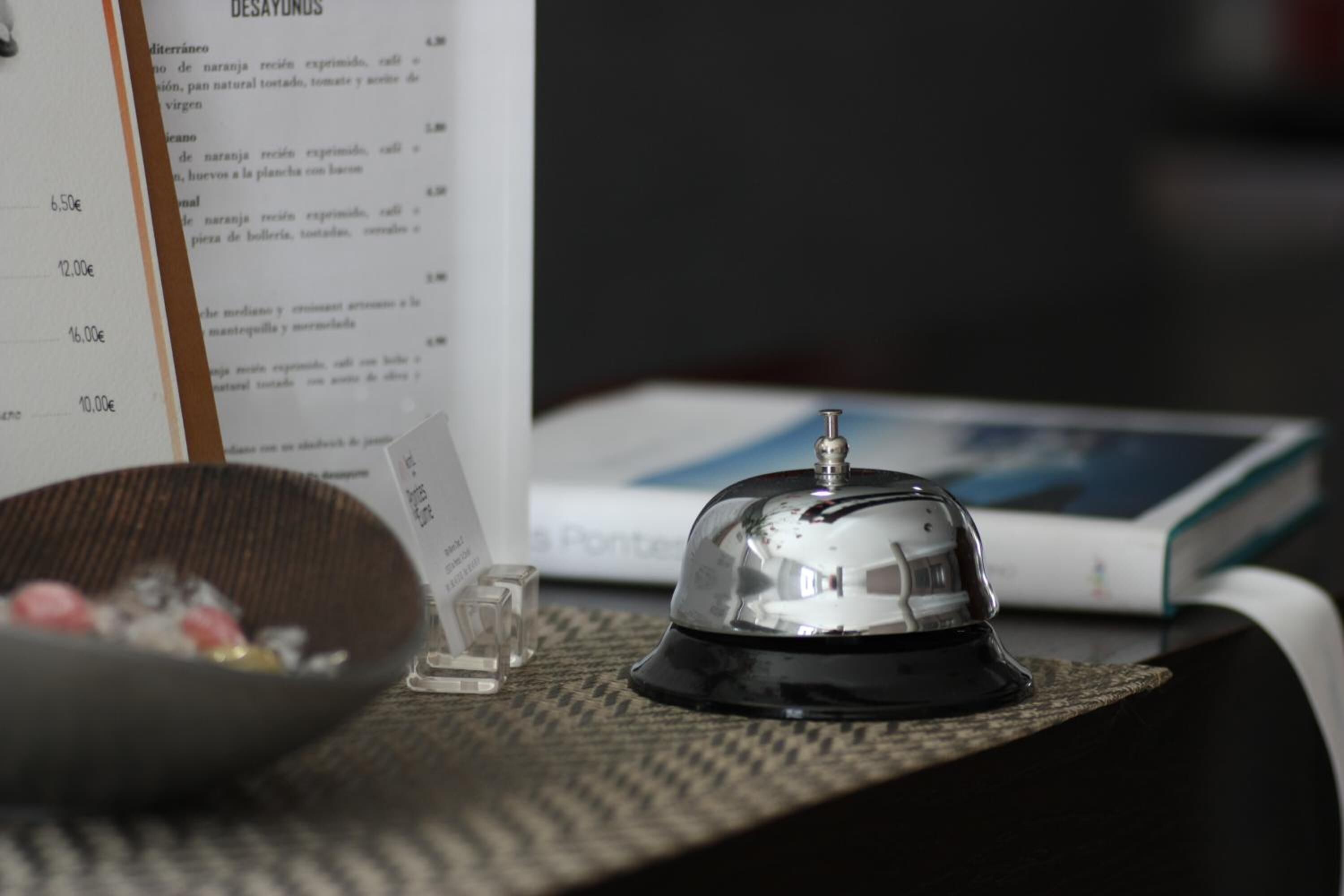 A hotel reception area with a bell, a menu, and a bowl of fruit on a table.