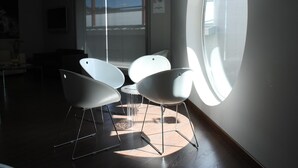 Habitació moderna amb tres cadires blanques, una taula petita i una finestra gran que deixa entrar llum natural.