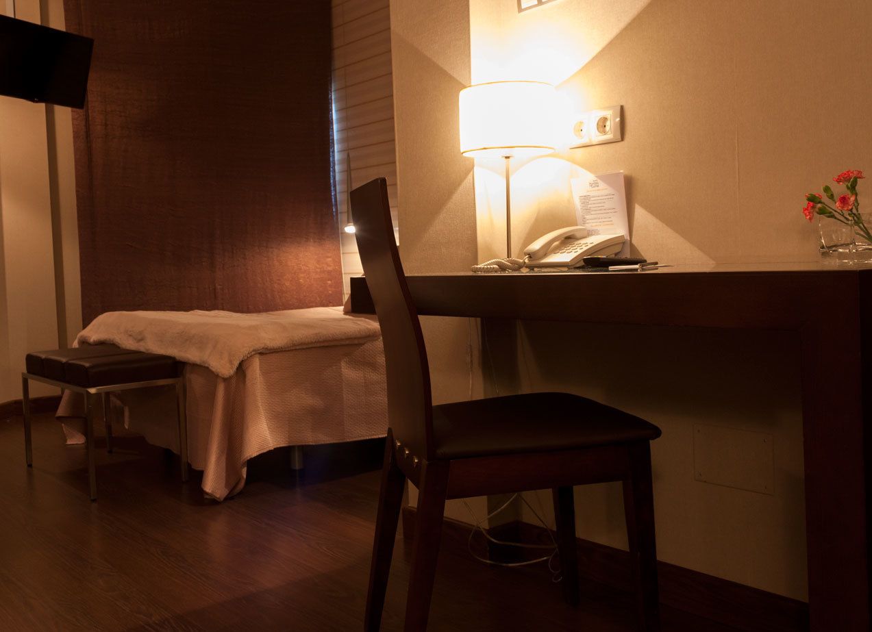 A hotel room with a bed, a desk with a lamp, and a chair.