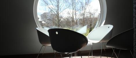 A room with a large round window, two modern chairs, and a view of trees and buildings outside.