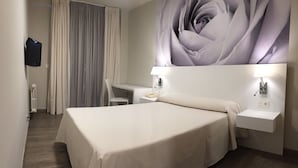 Una habitación de hotel con cama, escritorio, silla, televisión y una gran obra de arte floral en la pared.