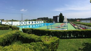 Una piscina con cubierta verde, rodeada de setos bien cuidados y una valla blanca con detalles azules.