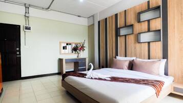 A hotel room with a large bed, a wooden accent wall, a desk with a mirror, and a vase with flowers.